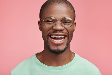 Portrait of cheerful successful male enterpreneur smiles broadly, wears round spectacles, happy to recieve triumph, being honored by colleagues and partners, has high profits and prosperous firm