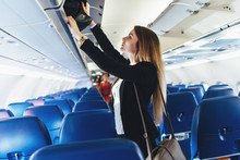 Female Student Putting Her Hand Luggage Into Overhead Locker On Airplane
