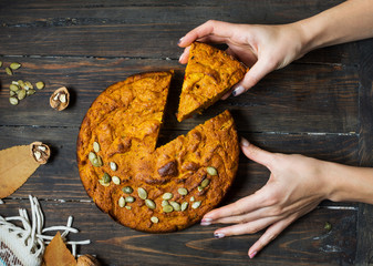 Female hands hold homemade Pumpkin Pie on rustic wood background.