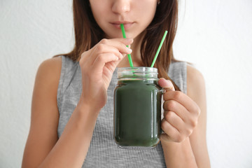 Wall Mural - Woman drinking spirulina cocktail on light background