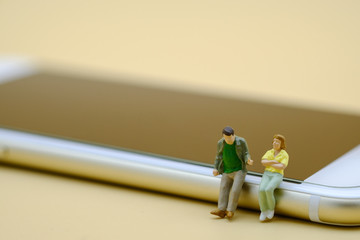 Technology and communication concept. Two miniature people figures sitting and talking on smart phone.