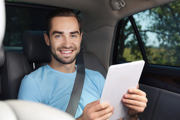 Young man with tablet on backseat of car