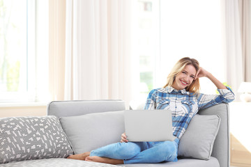 Sticker - Beautiful young woman with modern laptop on sofa at home