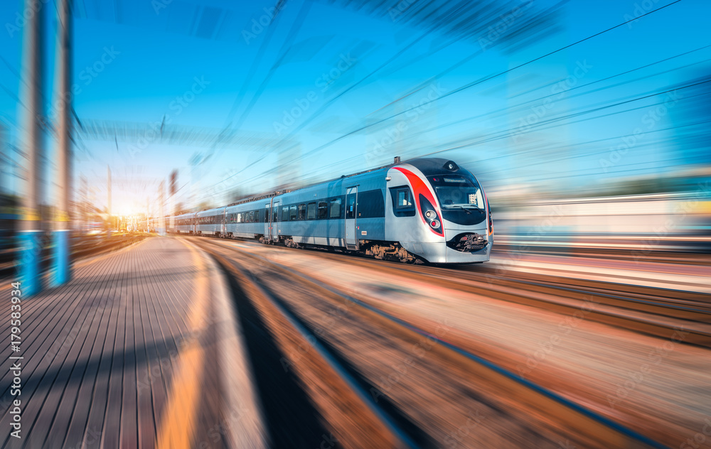 High speed train in motion at the railway station at sunset in Europe. Modern intercity train on railway platform with motion blur effect. Industrial landscape. Passenger train on railroad. Vintage - obrazy, fototapety, plakaty 