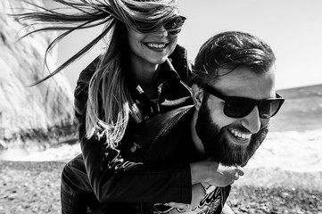 Black&white photo of happy couple in the leather jackets running on the beach