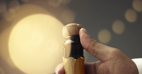 Wall Mural - Close up slowmotion video of man's hands opening a bottle of champagne on gray background with lights and flares