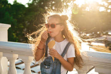 Preteen child girl wearing red sunglasses walking along city street and eating ice cream