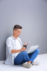 Canvas Print - Young man with laptop and mobile phone sitting on floor near grey wall