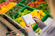 Woman with notebook in grocery store, closeup. Shopping list on paper.