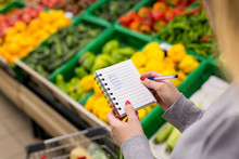 Woman With Notebook In Grocery Store, Closeup. Shopping List On Paper.