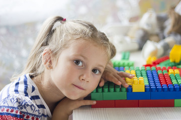 little girl in dress sits at table and collect the colored blocks