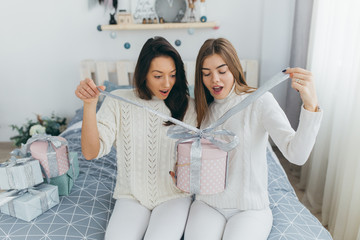 Wall Mural - Two happy, stylish and beautiful girl friends presented each other with Christmas gifts and opened them up in the vintage white room.