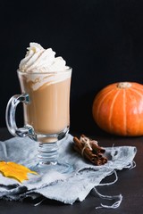 Wall Mural - Pumpkin spice latte or coffee with whipped cream, cinnamon and marshmallows in glass mug over black background. Vertical, copy space for text