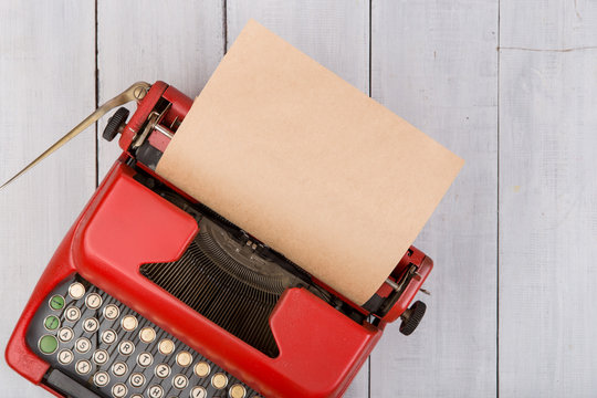 Red vintage typewriter with blank paper sheet on white wooden table