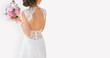 Beautiful bride on a gray background. On the bride is a long wedding dress with lace and an open back. Bouquet in hands.