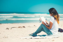 Young Woman Reading On Sandy Beach