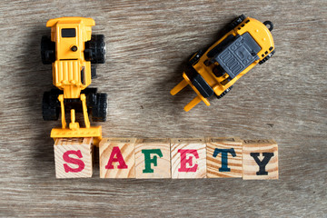 Poster - Toy plastic bulldozer hold toy block letter s to fulfill word safety with forklift on wood background