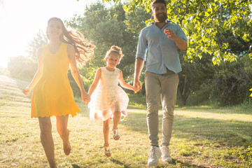 Two happy parents running together with their cute daughter