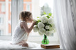© alexkich - A little girl is sitting on the windowsill. A bouquet of flowers