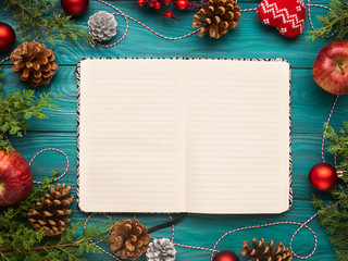 open notebook on christmas background with pine cones and ornaments. festive flat lay with white pag