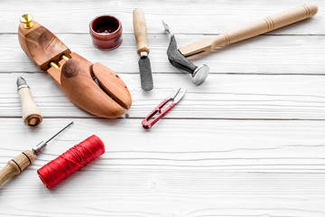 Tools for repair shoes. Wooden last, hammer, awl, knife, thread on white wooden background copyspace