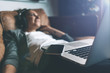 © Alex from the Rock - Attractive young happy woman listening to music in headphones with pleasure at coworking office, lying on sofa, using laptop and mobile phone and resting.
