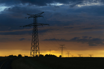 Wall Mural - High voltage power lines and transmission towers at sunset. Poles and overhead power lines silhouettes in the dusk. Electricity generation and distribution. Electric power industry and nature concept