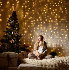 Young mother and her ittle daughters sitting near magical New year gifts by a Christmas tree