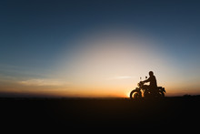 Silhouette Of Young Man Biker  And A Motorcycle On The Road With Sunset Light Background