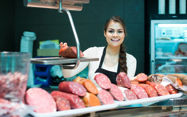 Wall Mural - Female butcher with wurst and bologna in meat store counter