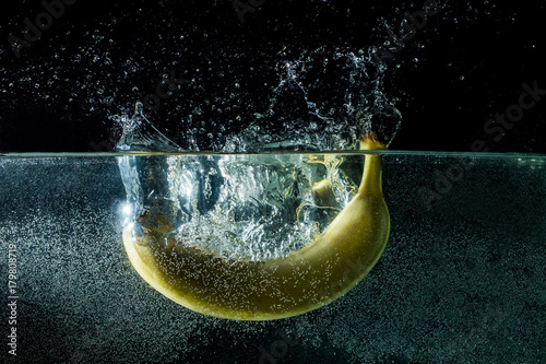 Zdjęcie XXL Banan spada w wodzie. Świeży banan z pluśnięciem na czarnym tle. banan zostaje trafiony strumieniem wody.
