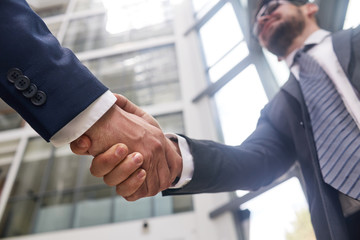 Firm handshake of business partners, interior of modern office lobby on background, close-up shot