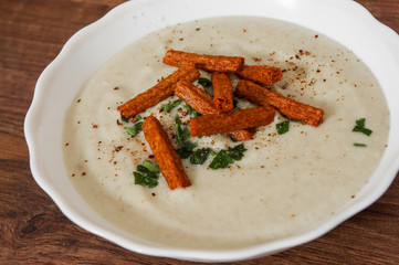 Mushroom cream soup with croutons, herbs and spices on a wooden background.