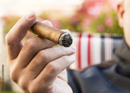 Fotografia Detail of the hand of a smoking man holding a burning cigar with a blurred backg