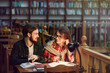 © proimagecontent - Portrait of two successful students casual stylish, boy and girl in library reading hall, evening time, education concept
