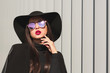 Glamorous brunette model in mirror glasses and broad brimmed hat posing near the shutters