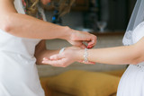 Fototapeta Pomosty - Girlfriend helps to dress the bride a bracelet on a hand befor wedding ceremony