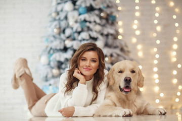 Beautiful young woman with a golden retriver dog near christmas tree