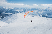 The Sportsman On The Paraglider Makes A Turn. Flies Over The Snowy Mountains