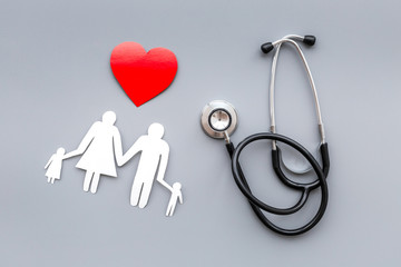  Take out health insurance for family. Stethoscope, paper heart and silhouette of family on grey background top view