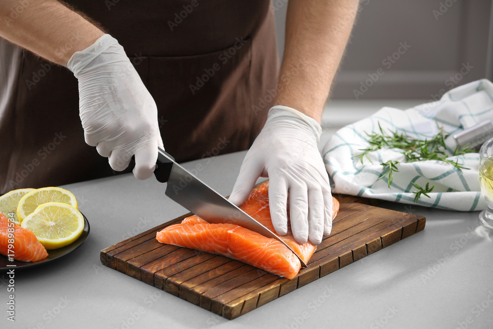 Man cutting fresh salmon fillet in kitchen