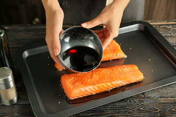 Wall Mural - Woman preparing salmon fillet with soy marinade on baking sheet