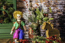 Rustic Christmas Scene With Antique Doll Sitting On Red Rocking Chair Next To Wood Horse Bouquet Of Winter Pine And Berries Green Shutter With Wreath And Brick Wall