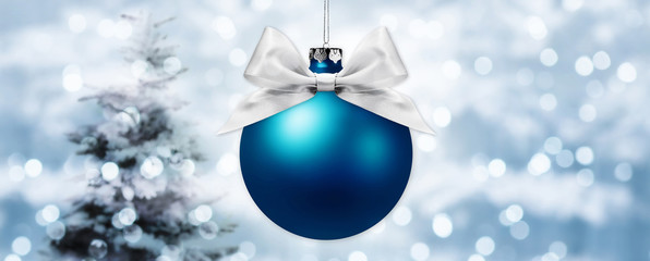 christmas ball with silver ribbon bow on blurred lights background with tree
