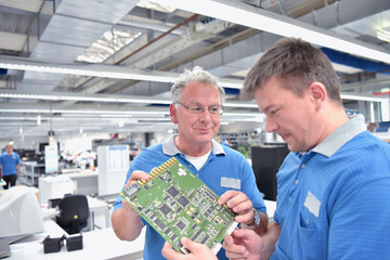 Teamwork: Techniker in der Elektronikfabrik bei Besprechnung über Fertigung von Platinen //  Technician in the electronics factory discussing the manufacture of printed circuit boards 