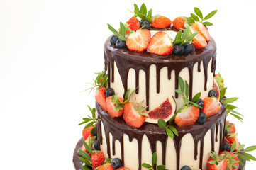 Wall Mural - Three-tiered wedding cake in chocolate, decorated with slices strawberries, blueberries, figs and green leaves on a white background. Picture for a menu or a confectionery catalog.