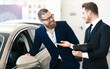 Smiling male buyer is listening to salesman in car dealership
