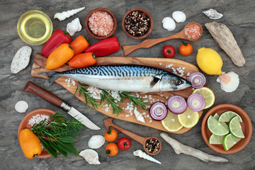 Mackerel fish health food with seasoning, vegetables and fruit on an olive wood board on marble background. High in omega 3 and beneficial for maintaining a healthy heart.