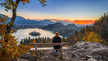 Bled, Slovenia - Red Hair Runner Woman Enjoying The Beautiful Autumn View And The Colorful Sunrise Of Lake Bled Sitting On A Hilltop Bench Wearing Black Pants And Jumper With Running Shoes