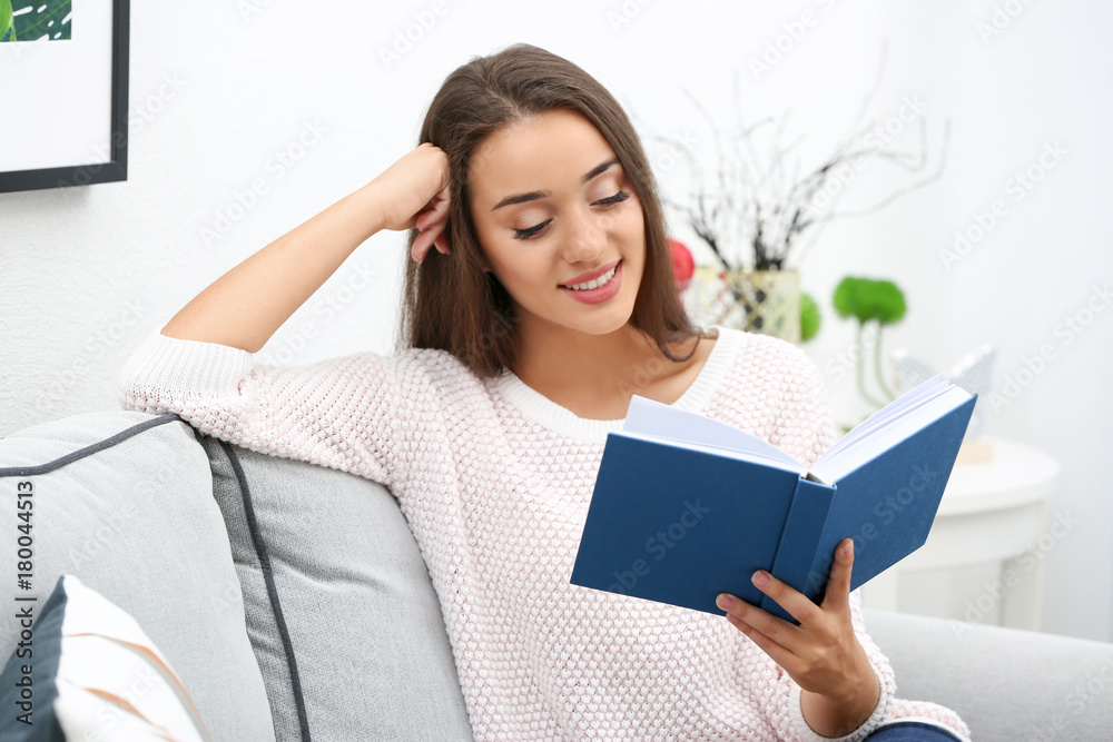 Young woman reading book on sofa at home